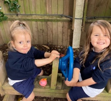 Two Peregrines Nursery girls sitting on a bench with steering wheels in the Forest School