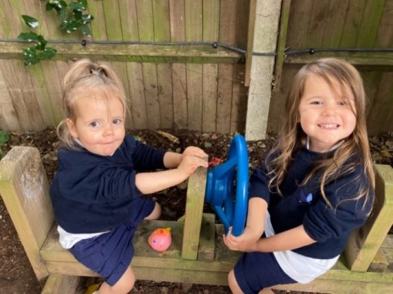 Two Peregrines Nursery girls sitting on a bench with steering wheels in the Forest School