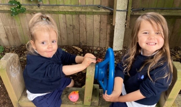 Two Peregrines Nursery girls sitting on a bench with steering wheels in the Forest School