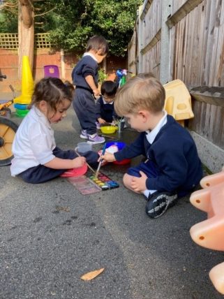 Young Peregrines Nursery children sitting down to draw on the playground floor